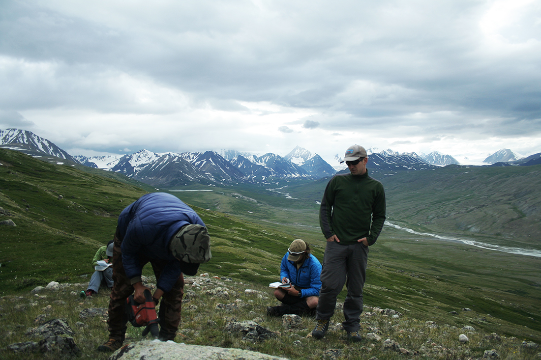 Oyungerel Sambuu, a student at the Mongolian University of Science and Technology, drills into a granite boulder for samples to trace the retreat of a glacier. The Potananin Glacier is visible in the distance. (Kevin Stark / Medill) 