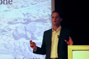 A man gives a science presentation, arms outstretched.