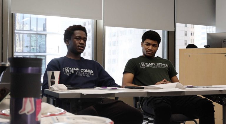 A photo of two students, seated at a desk, engaged in conversation.
