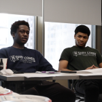 Two high school boys sit at a classroom table.
